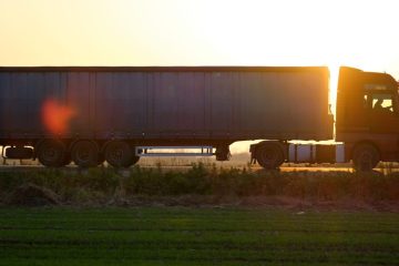 Semi-truck with cargo trailer driving on highway hauling goods in evening. Delivery transportation and logistics concept.